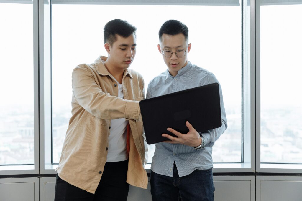 Two young professionals in an office setting, collaborating on a project using a laptop.